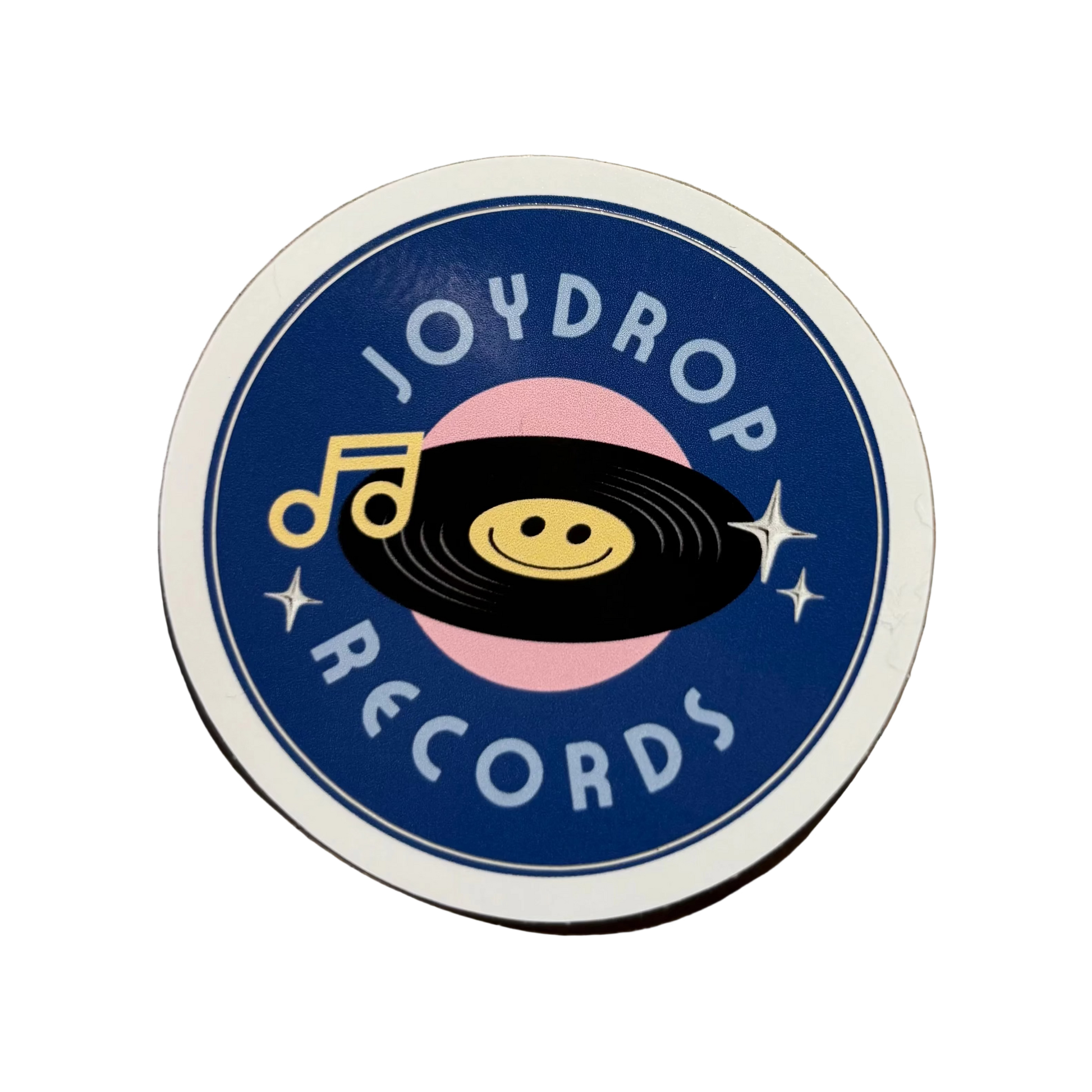A round vinyl record sticker for Joydrop Records, featuring a navy blue background, a pink record, a black vinyl disc with a yellow smiley face, and a yellow musical note.